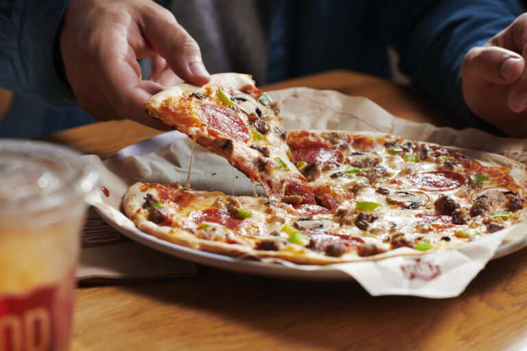 A slice of pizza with lots of toppings is grabbed from a plate holding a warm MOD Pizza.
