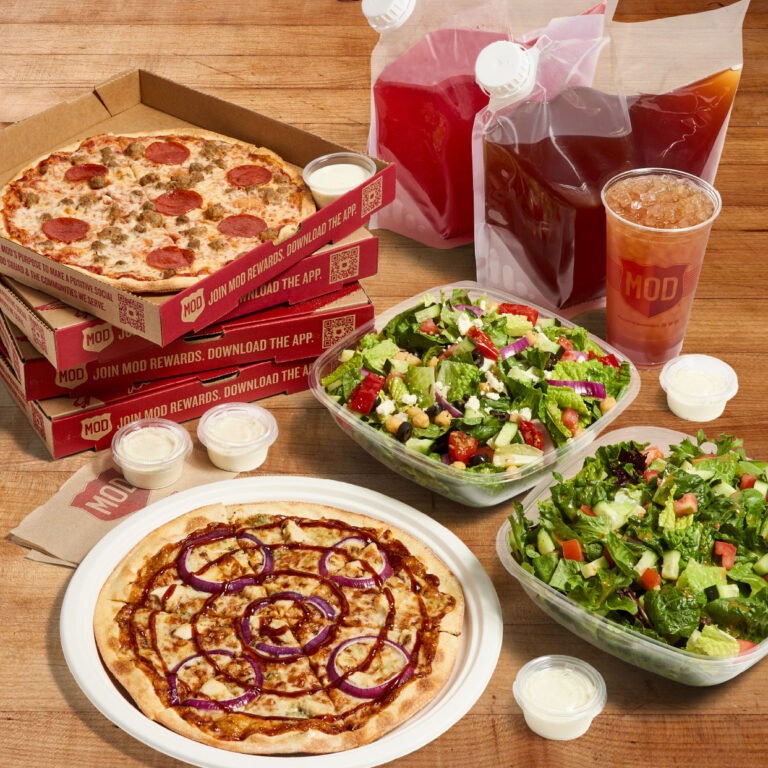 Pizzas in boxes, salads and beverages on a wood tabletop.