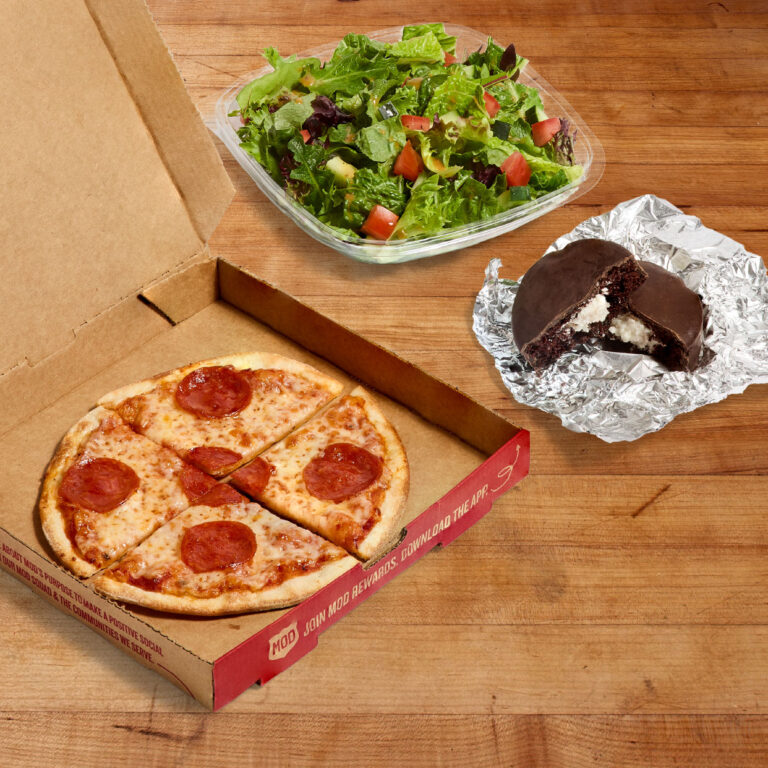 A mini pizza, salad and no name cake on a wood tabletop.